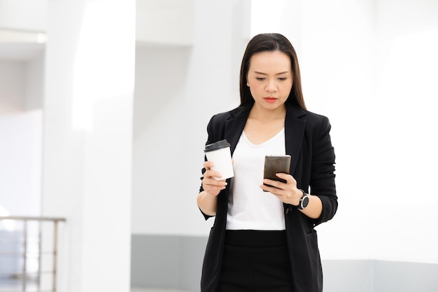 Portrait de réussite d'une femme d'affaires asiatique d'âge moyen tenant un téléphone intelligent et un café souriant à la caméra