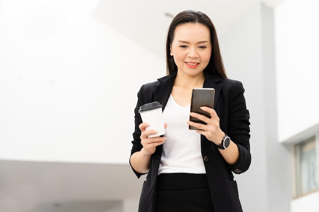 Portrait de réussite d'une femme d'affaires asiatique d'âge moyen tenant un téléphone intelligent et un café souriant à la caméra