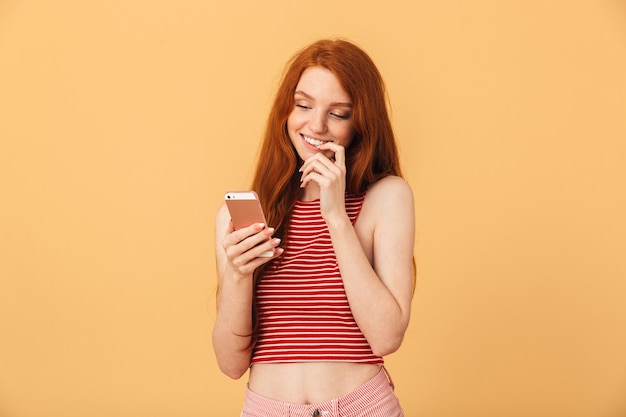 Portrait d'un rêve réfléchi heureux jolie jeune femme jolie rousse posant isolée sur un mur jaune à l'aide de la conversation sur téléphone portable.