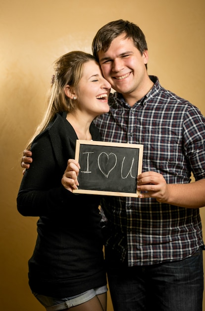 Portrait de rire couple amoureux tenant un tableau noir avec le mot écrit « Love »