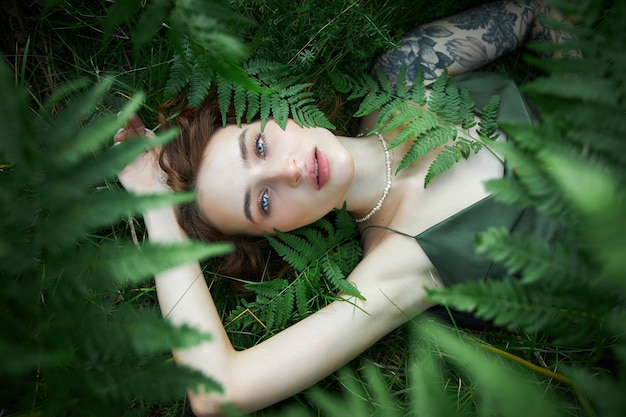 Portrait romantique d'une femme dans une fougère dans la forêt. Art femme maquillage naturel au repos dans la nature. Fourrés de fougères vertes