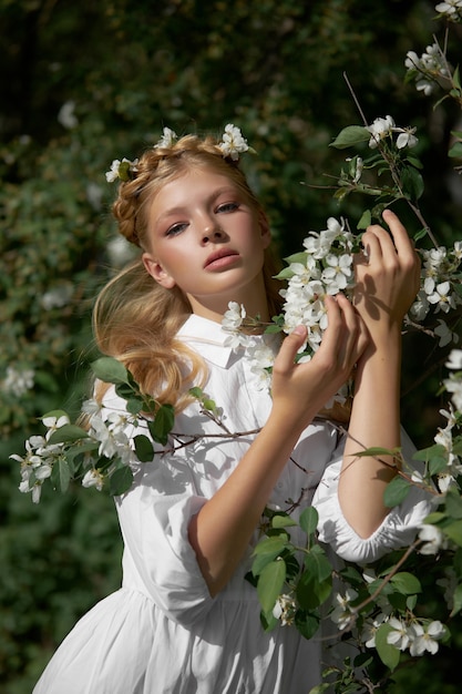 Portrait romantique d'une fille dans le parc près d'un pommier en fleurs. Cosmétiques naturels. Beauté naturelle d'une femme en robe blanche