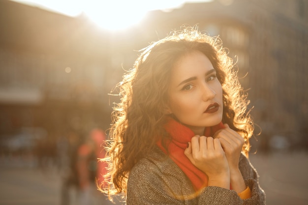 Portrait de rue du modèle brune glamour avec des lèvres rouges marchant dans la ville avec les reflets du soleil. Espace pour le texte