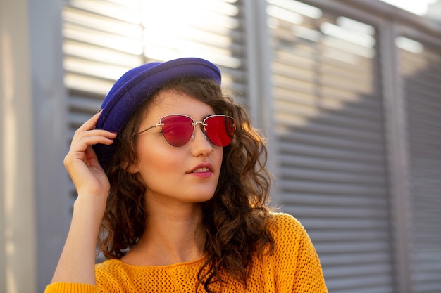 Portrait de rue d'une femme à la mode portant un chapeau bleu et des lunettes de soleil posant avec les reflets du soleil. Espace pour le texte