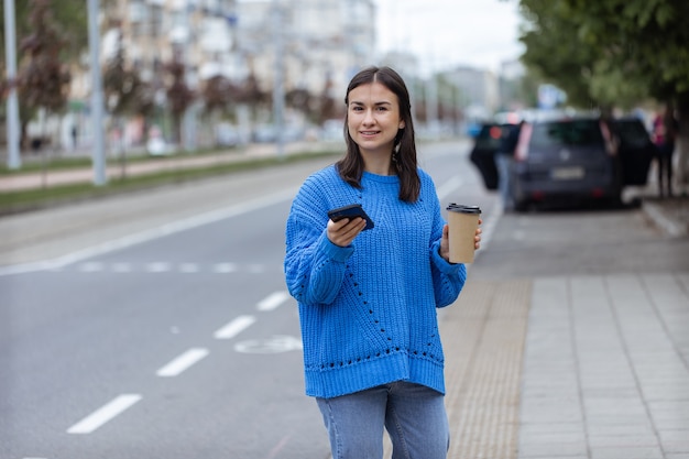 Portrait de rue d'une jeune femme avec un téléphone à la main et un café à emporter