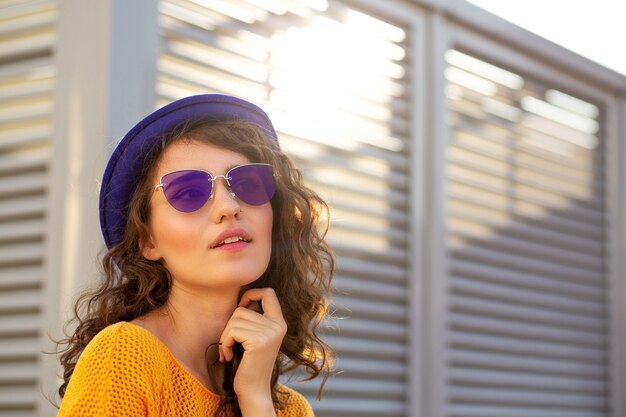 Portrait de rue d'une jolie femme portant un chapeau bleu et des lunettes de soleil posant avec les reflets du soleil. Espace pour le texte