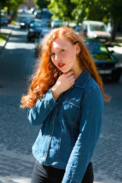 Portrait de rue d'un magnifique modèle aux cheveux roux aux cheveux bouclés dans les rayons du soleil