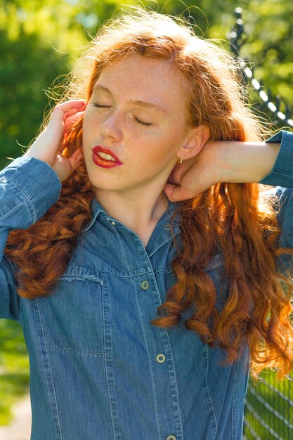 Portrait de rue d'un modèle attrayant aux cheveux rouges avec les yeux fermés posant dans le parc