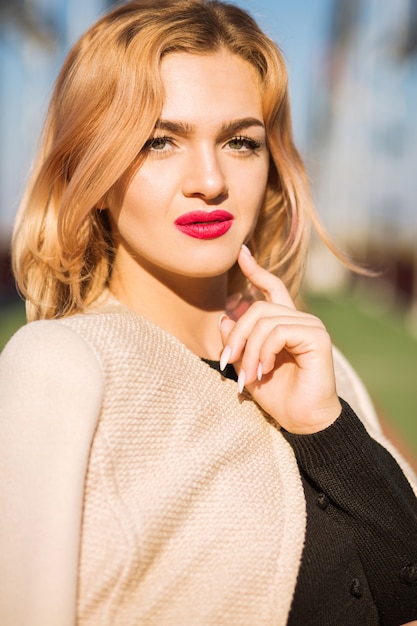 Photo portrait de rue d'un modèle blond élégant avec un maquillage lumineux et une peau parfaite posant à la lumière du soleil