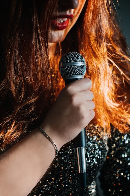 Portrait sans visage d'une femme rousse en robe de soirée scintillante tenant un microphone dans la nuit noire