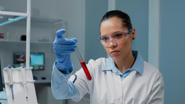 Portrait d'un scientifique de laboratoire analysant le sang d'un tube à essai sur un lieu de travail chimique. Chercheur médical faisant des expériences à l'aide d'un flacon avec une substance liquide rouge. Femme étudiant pour l'innovation