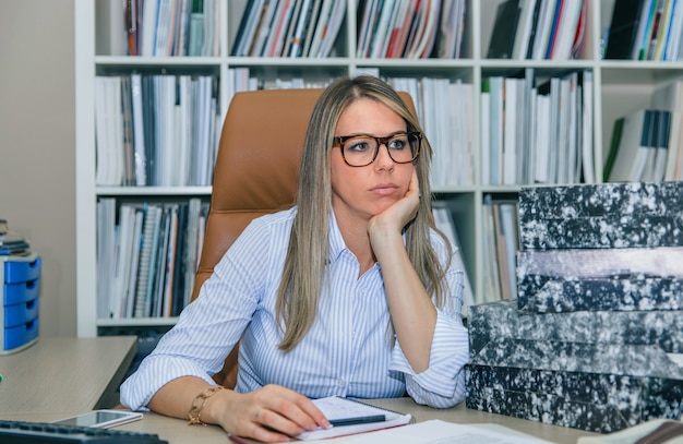 Portrait d'une secrétaire blonde ennuyée avec beaucoup de travail en attente sur son bureau