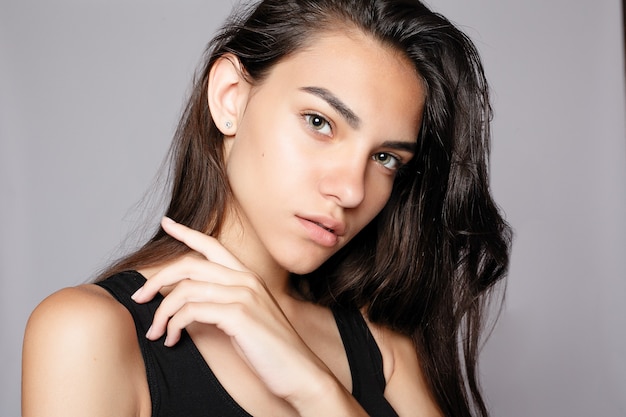 Portrait d'un séduisant souriant en regardant la caméra. Vêtue d'une robe noire. Posant sur fond gris. Belle femme souriante avec une peau propre, un maquillage naturel et des dents blanches