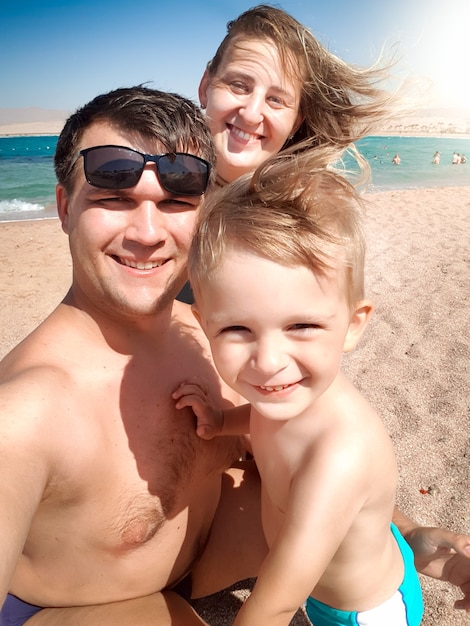 Portrait de selfie d'une famille joyeuse et souriante sur la plage de la mer au jour de vent ensoleillé. Se détendre en famille et passer du bon temps pendant les vacances d'été.