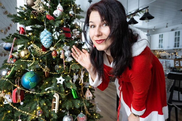 Portrait selfie d'une femme en robe de Père Noël rouge dans un intérieur de maison avec un arbre de Noël