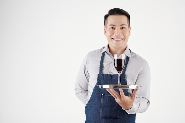 Portrait d'un serveur hospitalier souriant servant un verre de vin rouge isolé sur blanc