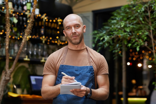 Portrait de serveur mature en uniforme est prêt à prendre l'ordre qu'il regarde debout au restaurant