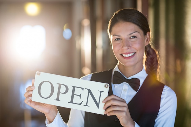 Portrait de serveuse souriante tenant une pancarte ouverte