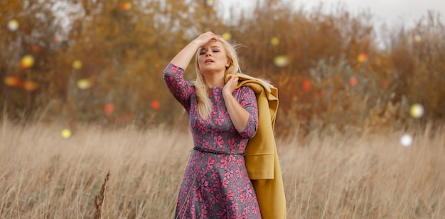 Portrait, de, sexy, belle femme, dans, robe rose, manteau jaune, maquillage yeux charbonneux, cheveux volants dans l'herbe sèche