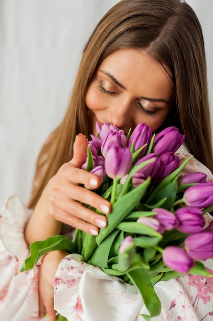 Portrait de sexy belle jeune femme aux cheveux longs Modèle avec un bouquet de tulipes lilas sur les vacances de printemps blanches