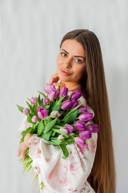 Portrait de sexy belle jeune femme aux cheveux longs Modèle avec un bouquet de tulipes lilas sur les vacances de printemps blanches