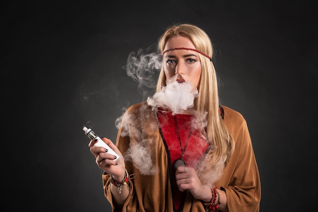 Portrait de sexy jeune hipster fumer vaping fille. La femme est habillée à la manière d'un bohème. Notion de vapeur. Vapoter une e-cigarette.