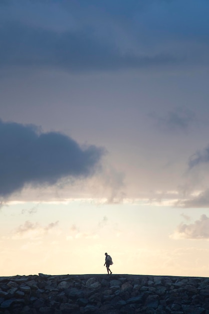 Portrait de silhouette d'homme avec filet de pêche marchant sur des rochers au soleil levant