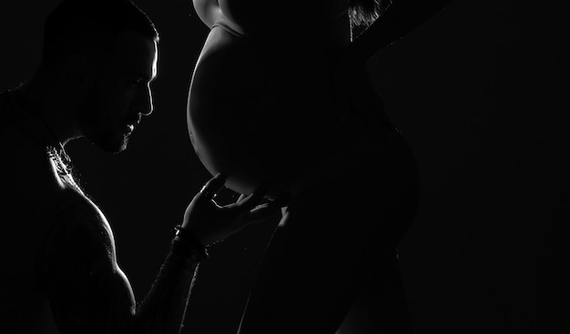 Photo portrait de silhouette mari homme embrassant le ventre d'une femme enceinte parents futurs mère et père attendant leur bébé concept d'amour jeune couple heureux famille attendant bébé isolé sur fond noir