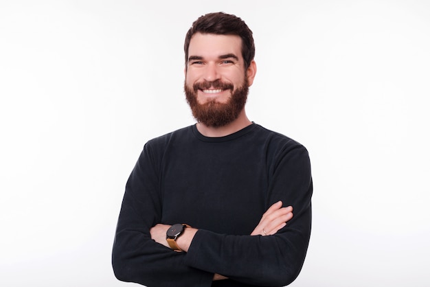 Portrait simple d'un jeune bel homme barbu souriant à la caméra portant un pull et croisant les bras.