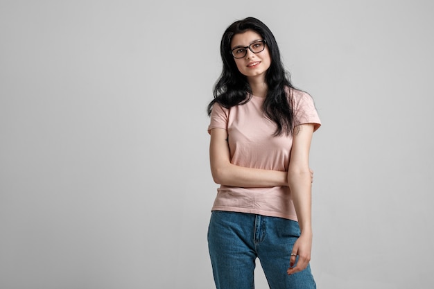 Portrait de smart belle fille brune à lunettes avec maquillage naturel, sur fond gris.