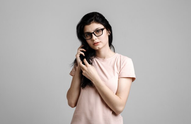 Portrait de smart belle fille brune à lunettes avec maquillage naturel, sur fond gris.