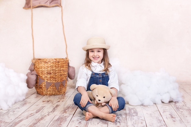 portrait smiling little girl sitting on wall of a balloon, stars and clouds and holding a teddy bear. fille joue dans la chambre des enfants avec un jouet. enfance. enfant détient un cadeau pour les vacances. anniversaire