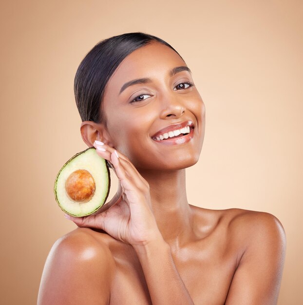 Portrait de soins de la peau et d'avocat avec une femme modèle en studio sur fond beige pour la beauté Visage de fruits et d'antioxydants avec une jolie jeune femme posant pour des cosmétiques bio ou naturels