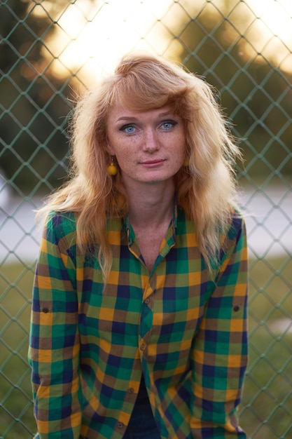 Portrait de soirée de rousse gingembre fille portée en chemise à carreaux et debout près de la clôture