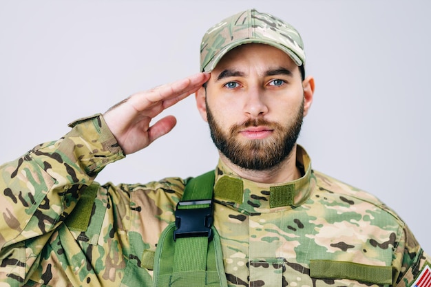 Portrait d'un soldat de l'armée américaine en uniforme de camouflage saluant en regardant la caméra Le soldat tient sa main sur sa tête en signe de respect