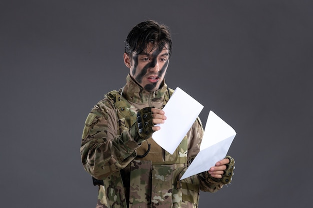 Portrait de soldat masculin en camouflage avec lettre sur mur sombre