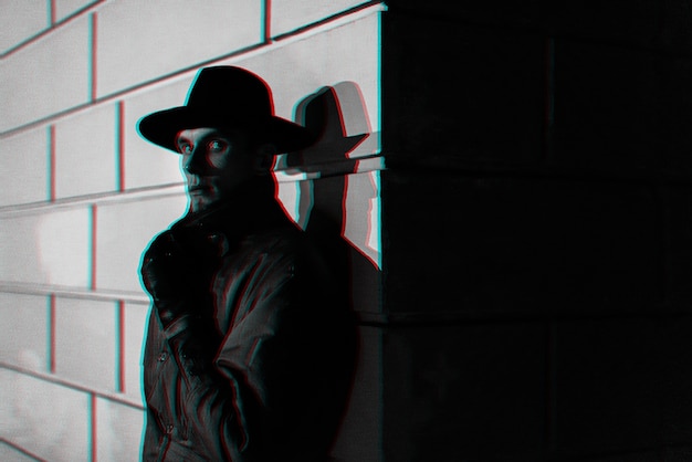 Portrait sombre d'un homme dans un imperméable avec un chapeau la nuit dans la rue. Noir et blanc avec effet de réalité virtuelle glitch 3D