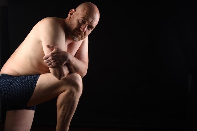 Photo portrait sombre d'un homme torse nu sur fond noir appuyé sur sa jambe