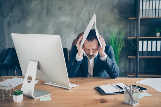 Portrait de son bel homme déprimé expert tenant un document papier sur la tête comme une affaire de droit sur le toit, l'économie du procès, l'assurance, la diminution de l'assurance à la station de travail du mur en béton industriel moderne