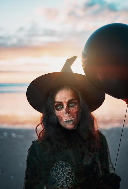 Portrait d'une sorcière au visage peint avec des ballons noirs au coucher du soleil à l'extérieur