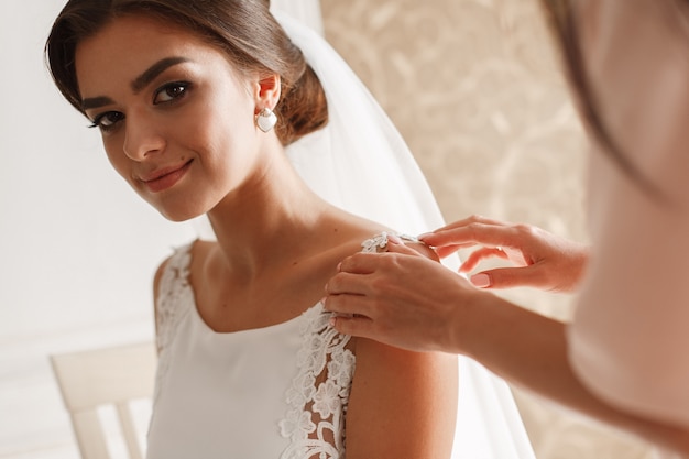 portrait souriant belle mariée en robe chic et voile intérieur dans la chambre d'hôtel