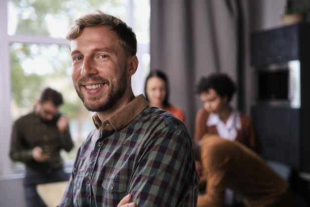 Portrait souriant homme d'affaires confiant debout dans une salle de bureau moderne avec les bras croisés divers collègues sur fond