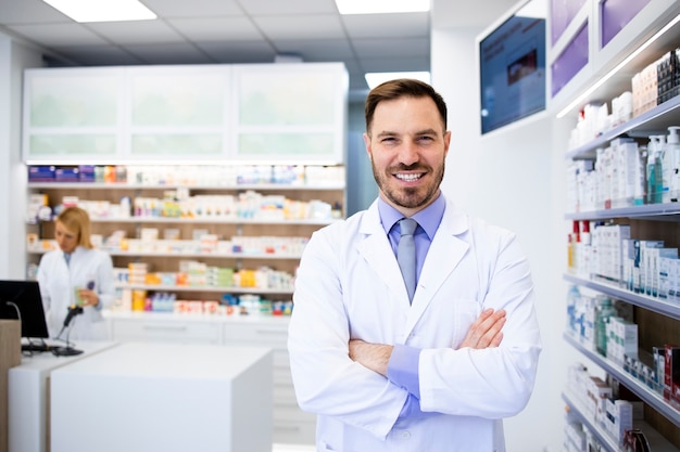 Portrait de souriant pharmacien caucasien debout en pharmacie avec les bras croisés.