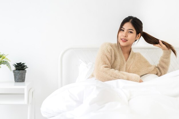 Portrait de souriante joyeuse belle jolie femme asiatique propre peau blanche fraîche et saine posant le sourire en vêtements de pyjama Fille abattant se détendre et profiter du temps sur le lit à la beauté homeasia