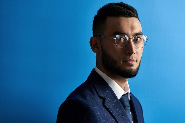 Portrait de sourire bel homme d'affaires asiatique kazakh réussi en costume et lunettes sur fond bleu studio isolé