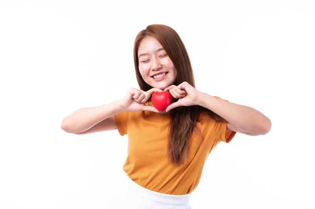 Portrait de sourire une belle jeune femme asiatique tenant un coeur rouge à la main sur fond blanc- concept de la Saint-Valentin