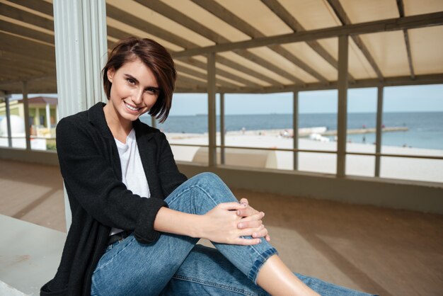 Portrait de sourire belle jeune femme assise dans la tonnelle au bord de la mer