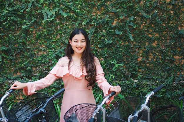 Portrait de sourire femme asiatique heureuse debout et tenant un vélo avec des feuilles de lierre vert frais sur le mur. activité de détente.