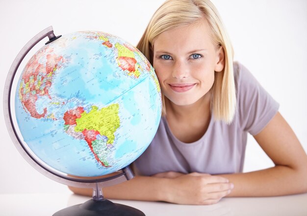 Photo portrait sourire et globe pour voyager avec une femme en studio sur fond blanc pour destination de vacances faites face à la terre ou à la planète avec une jeune personne heureuse regardant un endroit pour des vacances dans le monde