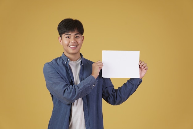 Portrait de sourire heureux joyeux jeune homme asiatique habillé avec désinvolture montrant du papier vide placard vide isolé.